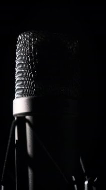Dikey, stüdyo mikrofonu arka planda siyah bir arkaplanda döner. Yüzeyinde krom ızgarası olan daha yoğun bir mikrofon. Konsept kayıt stüdyosu, ses, podcast, karaoke. Boşluğu kopyala