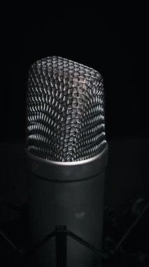 Dikey stüdyo mikrofonu siyah arka planda yakın planda döner. Yoğunlaştırıcı mikrofon ızgara yüzeyi etrafında dönüyor. Konsept kayıt stüdyosu, ses, yayın. Boşluğu kopyala, metin için yer.