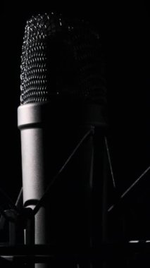 Stüdyo yoğunlaştırıcı mikrofon arka planda siyah bir arkaplanda dönüyor. Çevresinde dönen mikrofon yüzeyinin krom şebekesine yakın çekim. Konsept kayıt stüdyosu, ses, podcast, karaoke. Uzayı kopyala, Dikey