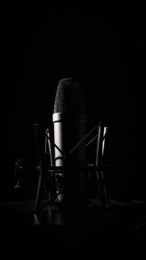 Dikey, stüdyo mikrofonu arka planda siyah bir arkaplanda döner. Yüzeyinde krom ızgarası olan daha yoğun bir mikrofon. Konsept kayıt stüdyosu, ses, podcast, karaoke. Boşluğu kopyala