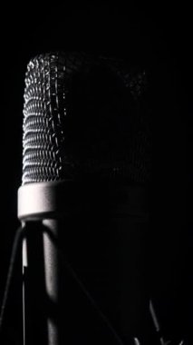 Stüdyo yoğunlaştırıcı mikrofon arka planda siyah bir arkaplanda dönüyor. Çevresinde dönen mikrofon yüzeyinin krom şebekesine yakın çekim. Konsept kayıt stüdyosu, ses, podcast, karaoke. Uzayı kopyala, Dikey