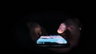 Adam sosyal medya haberlerini karanlık bir odada, geniş açılı, yakın plan bir telefondan aktarıyor. Tanımlanamayan birinin elleri. Akıllı telefon ekranında yazı yazıyor. Karanlıkta parlıyor..