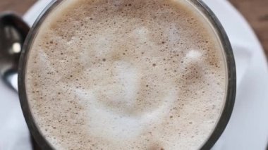 Ahşap bir kafe masasında duran karışık latte sanatının genel manzarası. Kahvenin ve köpüğün ılık tonları davetkar ve samimi bir his yaratıyor..