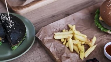 Altın patates kızartması ve peynirli ve marullu klasik bir burger tahtadan bir tahtanın üzerinde kahverengi kağıt üzerinde servis edilir. Sahne sıradan ve lezzetli bir yemeği çağrıştırıyor..