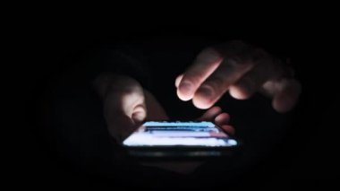 Erkek el, sosyal medya haberlerini karanlık odada, geniş açılı, yakın planda akıllı telefondan aktarıyor. Aydınlatılmış ekrana odaklanarak, düşük ışıklandırmalı bir ortamda bir kişi tarafından kullanılan telefonun özel görünümü.