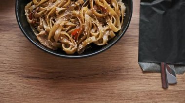 Susam tohumlarıyla kaplı tavuk, mantar ve dolma biberli udon eriştesi bir kafe masasında duruyor. Bu görüntü Asya mutfağını ve restoran ortamını göstermek için mükemmel.