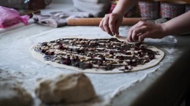 Kadınların elleri hamuru dikkatlice çikolatalı fındıklı ve meyveli rulo şeklinde sarıp ev mutfağında hamur işleri hazırlıyor.