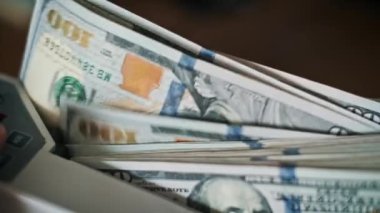 Ağır çekimde, bir para sayma makinesi titizlikle Amerikan doları banknotlarını işliyor, her bir banknotun içinden geçerken karmaşık detaylarını ortaya çıkarıyor..