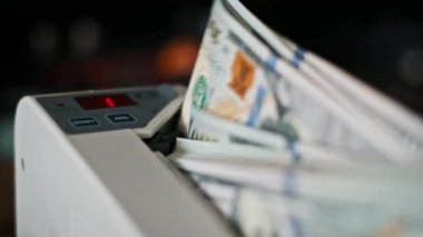Yakın çekim, özel bir makineyle Amerikan dolarlarının tam sayımını yakalıyor. Parlak kırmızı LED ekran açıkça artan toplam göstermektedir, hız ve doğruluğu vurguluyor