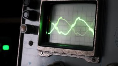 Antika bir osiloskop ekranı, analog teknolojinin ve elektronik ölçümün cazibesini vurgulayarak, koyu bir arkaplan üzerinde canlı bir yeşil sinyal dalgası görüntüler..