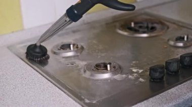 Yakın çekim buhar temizleyicisi yağlı bir gaz sobasını temizlemek için kullanılıyor. Güçlü buhar ve fırça bağlılığı etkili bir şekilde gevşetilir ve yanmış gıda ve kiri temizler, parlak bir son bırakır