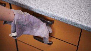 Temizlik eldiveni giyen biri mutfak dolabının çekmecesini ıslak bezle siler, mutfakta temizlik ve hijyen sağlar..
