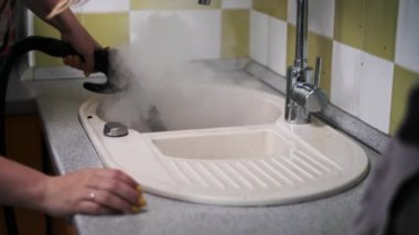Kadın kirli bir mutfak lavabosunu temizlemek ve sterilize etmek için el yapımı bir buhar temizleyicisi kullanıyor. Parlak bir sonuç için kiri ve bakteriyi temizlemeye odaklanıyor..