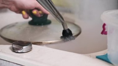 Mutfak lavabosundaki yağlı tavayı temizlemek için buhar temizleyicisi ve fırça eklentisi kullanan birinin yakın plan fotoğrafı..