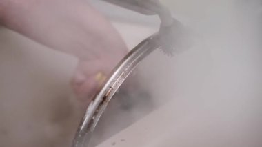 Mutfak lavabosundaki yağlı bir tavanın kenarını titizlikle temizleyen bir buhar temizleyicisi ile yavaş çekimde yakın plan çekimde buharın gücünü gösteriyor..