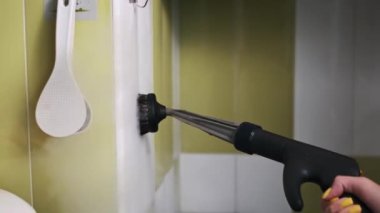 Bir insan, musluğun etrafındaki temiz mutfak fayanslarına titizlikle eklenmiş el yapımı buhar temizleyicisi kullanır, kiri temizler ve hijyeni sağlar..