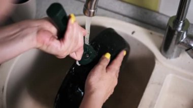 Kadın mutfak lavabosunda yanan bir tavayı özenle yıkıyor. İnatçı besin kalıntılarını temizlemeye çalışıyor..