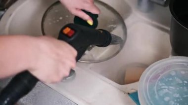 Kadınların elleri mutfak lavabosundaki el yapımı buhar temizleyicisiyle yağlı bir tavayı temizliyor..