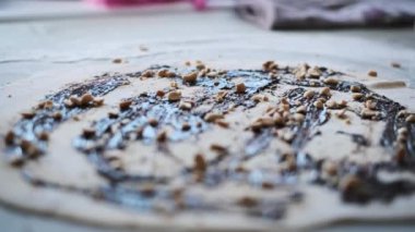 Bir ev mutfağında tatlı ve fındıklı bir hamur üzerine serpiştirilmiş çikolata dolgusuna fındık eklenen bir insan eli yakından görülüyor..