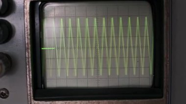 Bir el, vintage osiloskopun düğmesini nazikçe ayarlar ve ekrandaki yeşil dalga şeklini değiştirir. Bu büyüleyici görüntü analog teknolojinin dokunsal hassasiyetini gösteriyor..