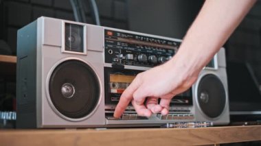 Bir el klasik bir teyp üzerindeki çalma butonuna basar, kaseti etkinleştirir ve geçmişin seslerini hayata geçirir..