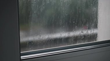 Pencereden süzülen yağmur damlalarının büyüleyici makro görüntüleri. Bulanık yeşil arka plan bu barışçıl ve atmosferik 4K videoya doğanın bir dokunuşunu ekler..