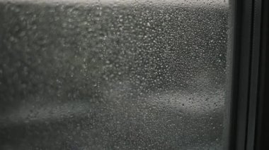 Pencere ekranına yapışan yağmur damlalarının yakın plan görüntüsü bulanık bir arkaplan karşısında desenli desen oluşturur.