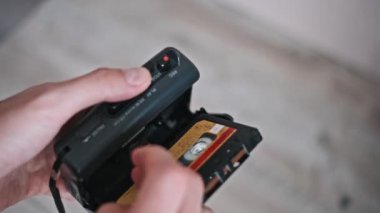 Bir adamın elinin portatif bir kasetçalara eski bir ses kasedi yerleştirirken yakın plan görüntüsü, süreci ve dokunsal deneyimi vurguluyor..