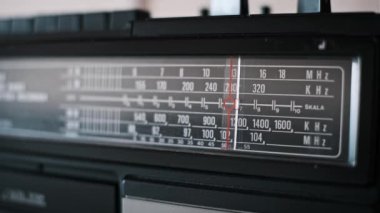 Sinyal arayan klasik bir radyo kanalına yakın çekim yapın. Kırmızı çizgi frekans ölçeğinde süzülüyor, beklenti ve nostalji hissi uyandırıyor..