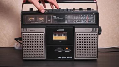 Adamın biri ses kasetini antika bir müzik kutusuna yerleştiriyor ve eli tuşları ayarlıyor. Bu nostaljik sahne, analog müzik dinlemenin ve eski moda teknolojinin çekiciliğinin özünü yakalıyor..