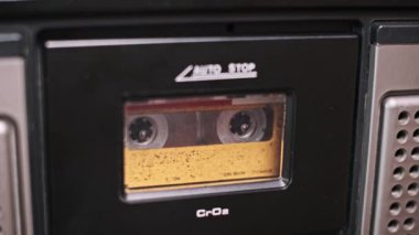 Eski bir müzik kutusunun içindeki ses kasetini yakından çek. Kasetler tozlu pencereden görülebiliyor, karışık kasetler ve analog ses çağına dair nostalji hissi uyandırıyor..