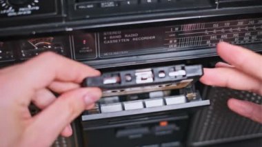 Bu ikonik müzik çaların ve analog teknolojinin nostaljisinin dokunsal doğasını vurgulayarak, bir elin dikkatlice ses kasetini antika bir müzik kutusuna yerleştirirken yakın plan çekimi..