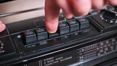 Eski bir teybin tuşları ile etkileşime giren bir elin yakın plan görüntüsü, bu retro müzik çaların ve analog kontrollerin cazibesinin dokunsal deneyimini gözler önüne seriyor.