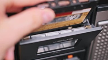 Eski bir müzik kutusuna ses kaseti yerleştiren bir elin yakın plan çekimi. Bu nostaljik sahne klasik analog teknolojinin dokunsal deneyimini yakalar..