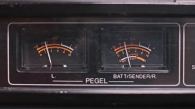 Eski tip teyp VU metrelerin yakın çekimi, iğneleri ritmik olarak dans ediyor, analog ses seviyelerini gösteriyor. Sesin görsel bir temsili ve analog teknoloji günlerine bir geri dönüş..