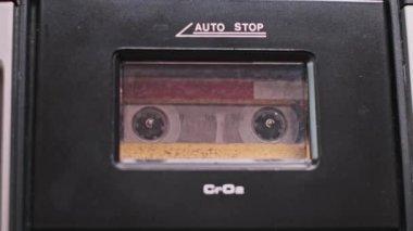 Bir parmak klasik bir teybin çalma tuşuna basar ve kaseti hayata geçirir. Yakın çekim, bu klasik cihazdan müzik sesi duyma beklentisini yakalar..