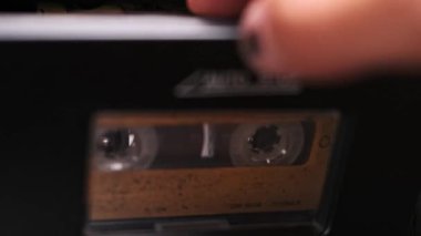 Bir el, müzik kaynağını yakalayıp nostaljik deneyimi durduran klasik bir teyp kasetini nazikçe çıkarıyor..