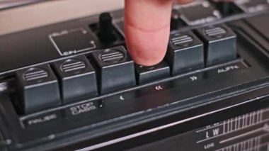 Parmak geri sarma düğmesine basar, sonra da klasik teyp üzerindeki durdurma düğmesine basar, kasetçalar üzerindeki dokunsal kontrolü vurgular. Analog ses teknolojisini takdir edenler için bir nostalji.