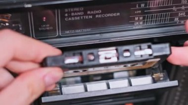 Bir el dikkatle klasik bir kaseti müzik çalmaya hazır bir teybe yerleştirir. Yakın çekim analog teknolojinin dokunsal deneyimini ve nostaljik çekiciliğini vurguluyor..