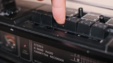 Bir parmak çalma tuşunu çalıştırır, sonra da klasik bir teybin durdurma tuşuna basar, bu da müzik çalmayı kontrol ettiğini gösterir. Bu yakın plan görüntü, analog ses teknolojisinin nostaljisini çağrıştırıyor..
