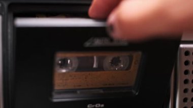 Bir elin, klasik bir teybe ses kaseti yerleştirdiği yakın plan bir fotoğraf. Eylem, geçmişte kalmış müzik dinleme ve analog teknoloji çağını anımsatıyor..