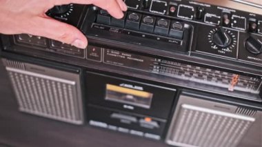 Bir el klasik bir teybin fırlatma tuşuna basar ve içindeki kaseti ortaya çıkarır. Bu yakın çekim, medyayı klasik bir müzik çalarından çıkarmanın basit eylemini yakalar.