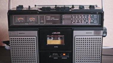 Bir el, antika bir teybin düğmeleriyle bir kaset yerleştirip analog teknolojinin ve geçmiş dönemin nostaljisinin dokunsal bağlantısını vurguluyor..