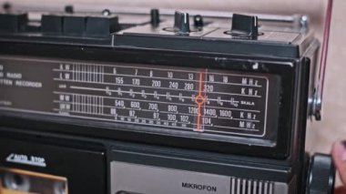 Bir el klasik bir radyo kadranını dikkatlice ayarlar ve parazitin arasında net bir sinyal arar. Görüntü, radyonun müziğin ve eğlencenin ana kaynağı olduğu bir dönemde nostalji hissi uyandırıyor.