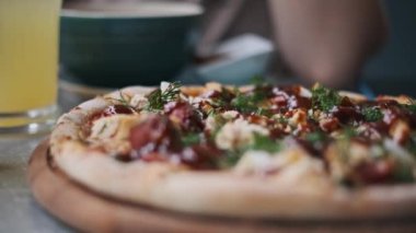 Ahşap bir tahtanın üzerinde BBQ tavuk pizzası latte, limonata ve arkada çorba. Bir kadın kafeterya masasında yemek yemekten hoşlanır..