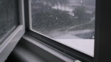 Şiddetli yağmur açık bir pencereden yağar ve şehir caddesini bulanıklaştırır. Karamsar ve atmosferik bir sahne oluşturur.