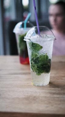 Kafedeki ahşap bir masada buzlu ve naneli iki bardak mojito kokteyli. Dikey çekim.