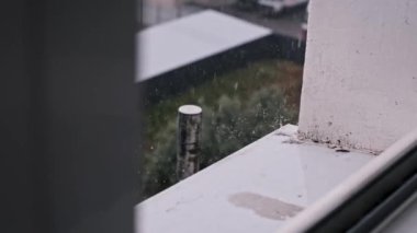 Yağmur damlaları pencerenin kenarına şiddetli bir şekilde düşer ve aşağıdaki caddenin manzarasını bulanıklaştırır. Sağanak yağış sırasında kapalı bir yerde korunma hissi yaratır..