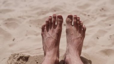 Güneşli bir yaz gününde, erkek ayağının göl kenarındaki kumsalda dinlenmesi. Tatil ve boş zaman kavramı.