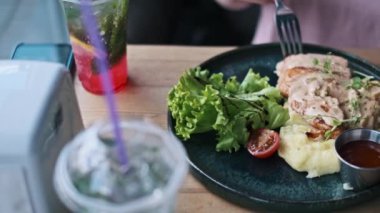 Bir kafede patates püresi, taze salata ve kiraz domatesli nefis tavuk göğsü yiyen bir kadın. Masada iki bardak taze mojito kokteyli..